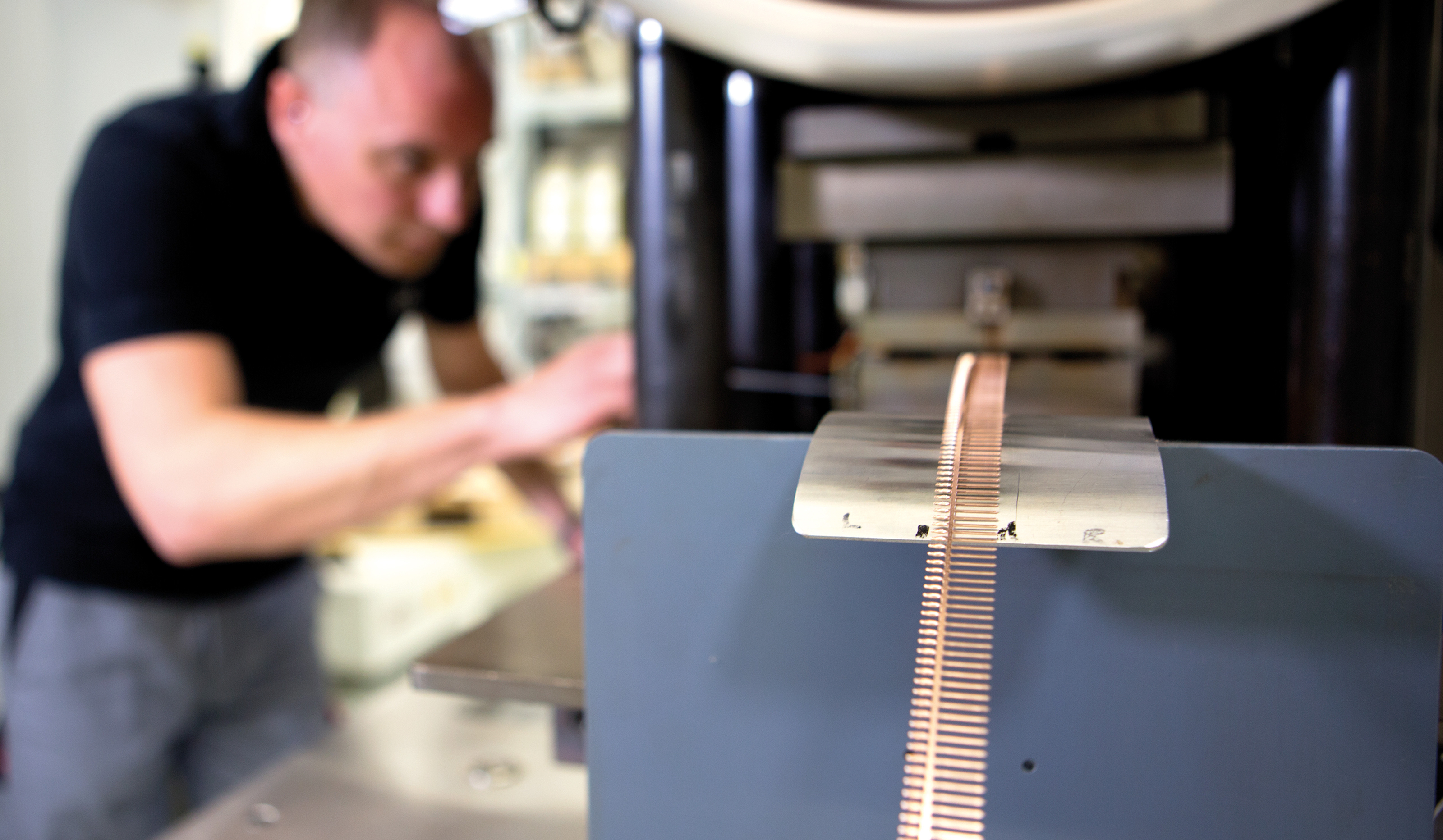 Auf dem Bild ist ein Mann zu sehen, der an einer Maschine arbeitet, die eine dünne Metallstreifenform bearbeitet.